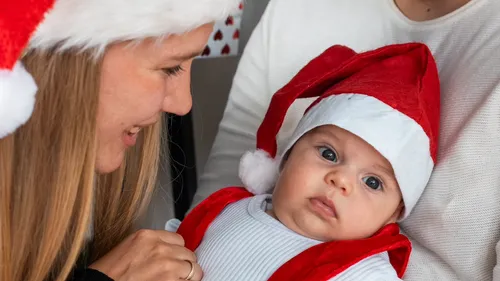 Baby mit Weihnachtsmütze, gehalten von einer lächelnden Frau