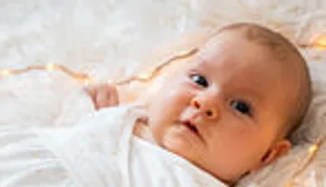 Baby lying on soft blanket, lights behind.