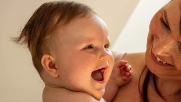 Laughing baby held by smiling adult.