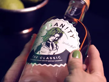 Eine Flasche wird gehalten, mit einer grünen Limette im Hintergrund.