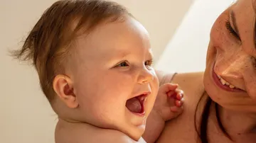 Smiling baby held by a happy woman.