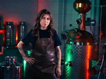 Woman stands next to a shiny still in a brewery.