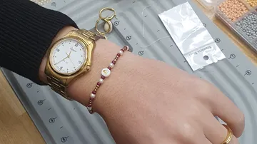 Hand mit Uhr und rotem Perlenarmband.