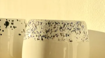 Speckled ceramic mugs against a light wall.