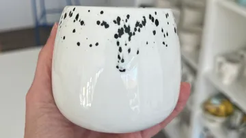 Person holding white speckled ceramic mug indoors.