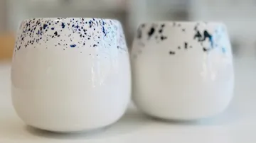 Two white ceramic cups with blue speckled design.