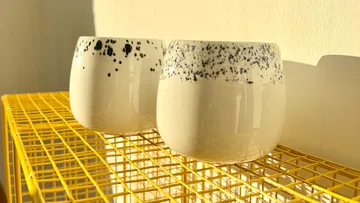 Two white speckled cups on yellow shelf.