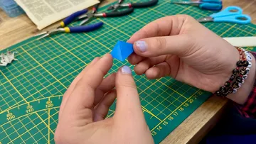 Hands folding blue origami on cutting mat.