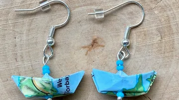 Origami boat earrings with map design, wooden background.