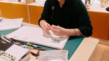 Person, die am Schreibtisch mit Malutensilien bastelt.