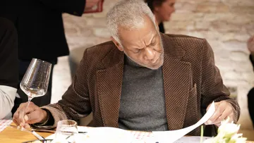 Man holding wine glass, reading menu at restaurant.