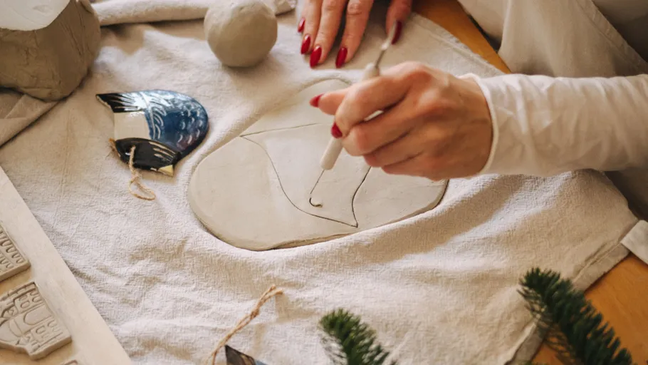 Person carving design into clay on table.