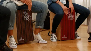 Zwei Leute spielen drinnen Cajón-Trommeln.