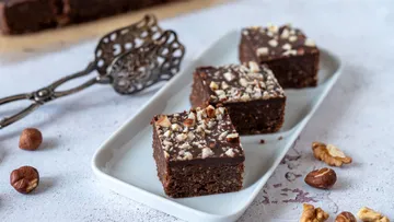 Drei Brownies mit Nussüberzug auf einem rechteckigen Teller.