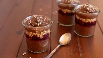 Drei Schokoladenpudding mit Beeren und Samen in Gläsern.