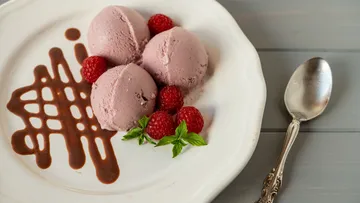 Himbeereis mit Sauce und Himbeeren auf einem Teller.
