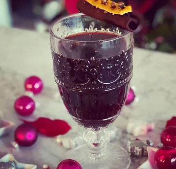 Dekoratives Glas Glühwein mit Beilagen, umgeben von Ornamenten.