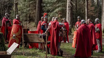Römische Soldaten in roten Umhängen stehen im Wald.