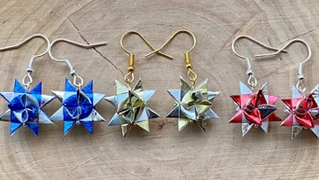 Stern-Origami-Ohrringe in Blau, Gold, Rot auf Holz.