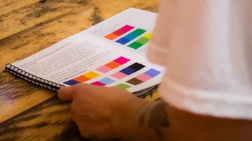 Person reading a color theory book on a wooden table.