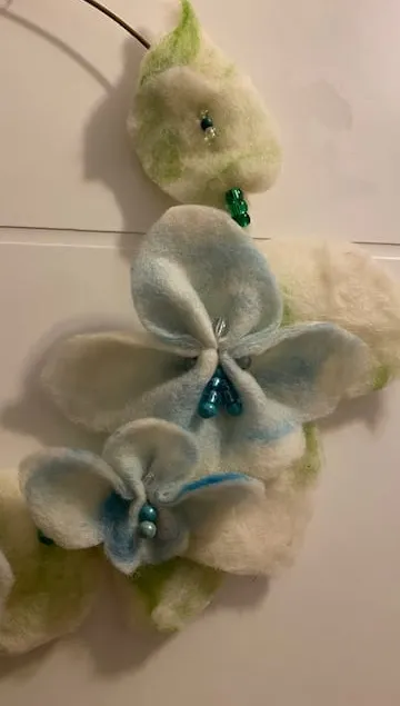 Blumendekoration aus Filz mit Perlen auf weißer Oberfläche.