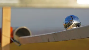Balancieren einer Metallkugel auf einer gekrümmten Holzoberfläche.