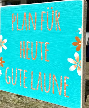 Wooden sign with 'Plan für heute gute Laune' text.