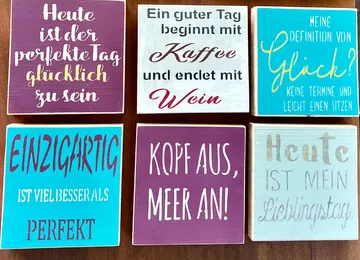 Sechs bunte Holztafeln mit deutschen Redewendungen.