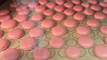 Pink macarons baking on silicone mat.