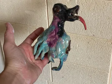 Hand holding colorful ceramic creature sculpture.
