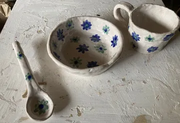 Handmade ceramic bowl, cup, and spoon with floral design.