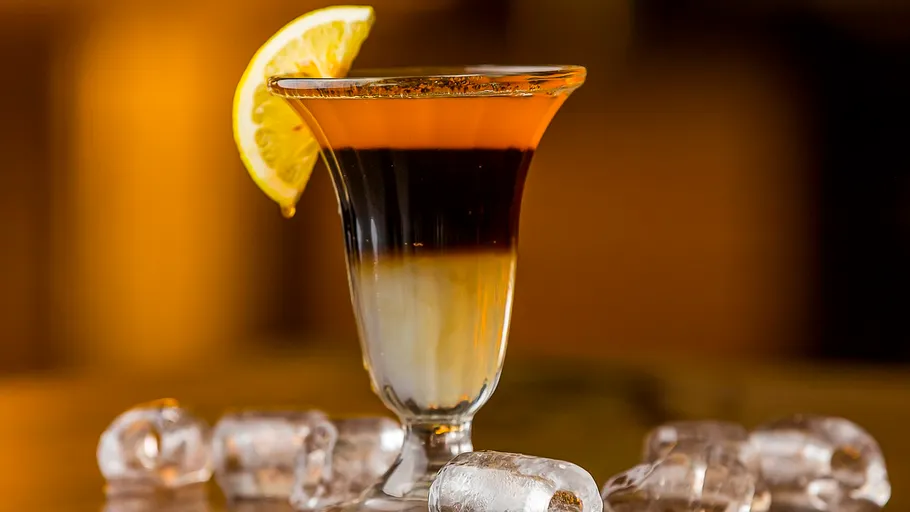 Layered cocktail with lemon slice on rim.