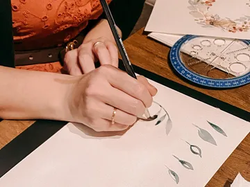 Eine Hand zeichnet dekorative Blätter auf Papier.