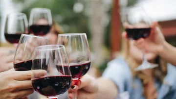 Hands clinking red wine glasses outdoors.