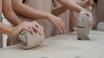 Hands shaping clay on a table.