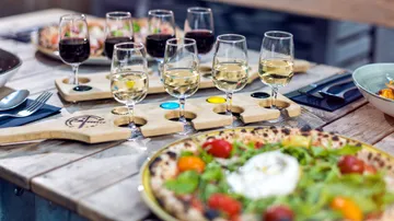 Weinflug und Pizza auf Holztisch.