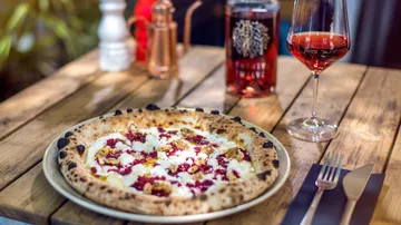Pizza mit Belag auf einem Holztisch mit Wein.
