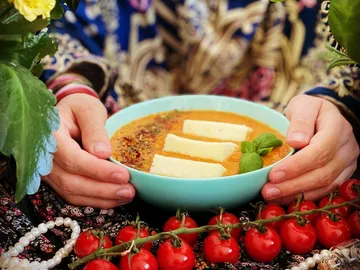 Eine Schüssel Suppe wird von Händen gehalten, umgeben von Kirschtomaten.