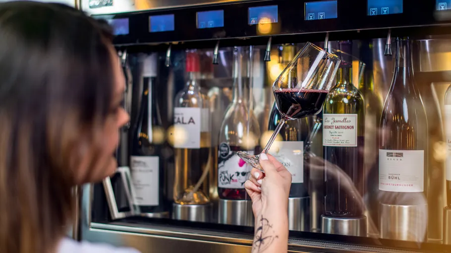 Person holding red wine glass by dispenser.