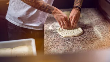 Person shaping pizza dough on countertop.