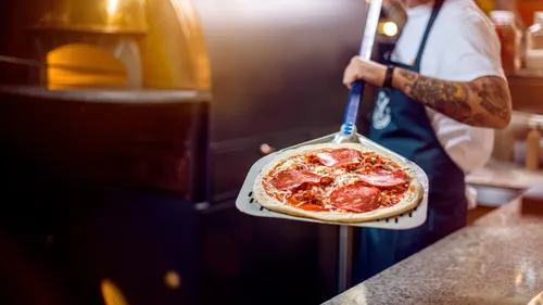 Koch legt Pizza in den Holzofen.