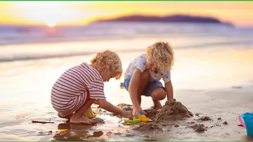 Two children building sandcastles on a beach at sunset.