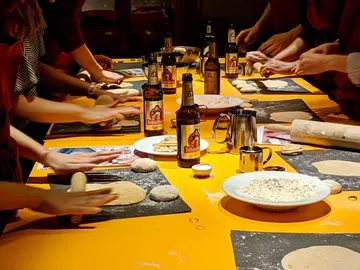 Menschen kneten Teig an einem sonnigen Tisch mit Bier.