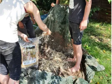 People fill a bag with hay in the garden.