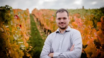 Man stands smiling in vineyard with autumn foliage.
