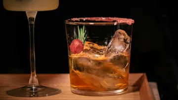 Whiskey cocktail with ice on wooden tray.