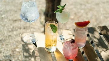 Five cocktails on wooden table outdoors.