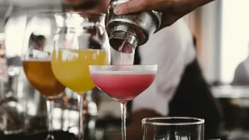 Bartender pouring pink cocktail into glass.