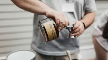 Person pouring whiskey into jigger outdoors.