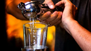 Hands squeezing citrus juicer over glass.
